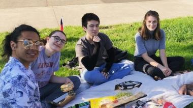 4 students sitting enjoying a picnic and smiling at the camera.